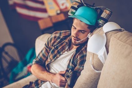 Passed out after great party. Young handsome man in beer hat napping on sofa in messy room after party