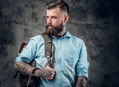 Portrait of stylish beard, male with tattoos on his arms and neck with backpack on his back.